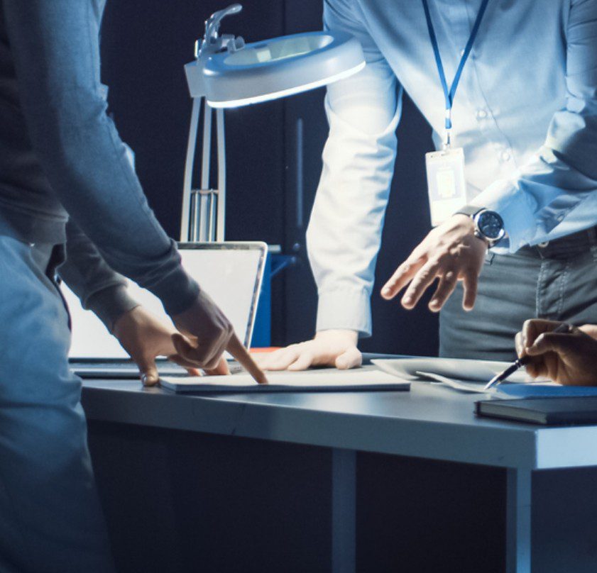 Photo of men wearing lanyard with photo ids on their necks discussing a document on a table