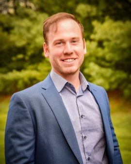 Headshot photo of Mr. Chase Harker wearing a navy blue suit with a grey shirt underneath