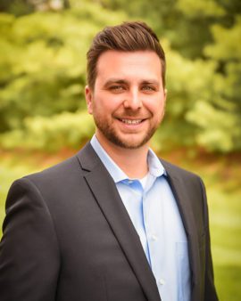 Headshot photo of Mr. Daniel Loy wearing a black suit and blue dress shirt underneath