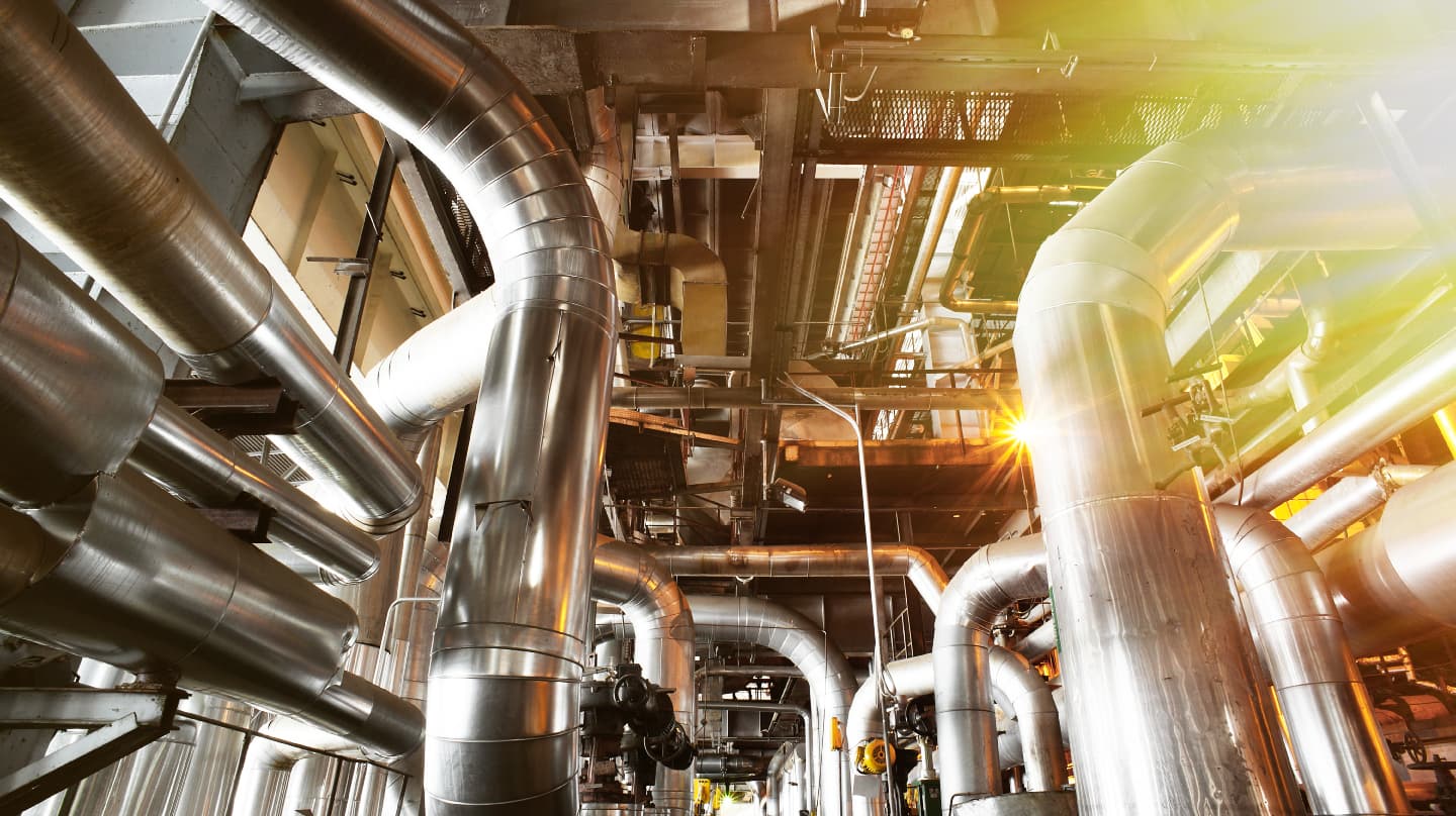 An industrial facility with an intricate network of large, shiny metal pipes running in various directions